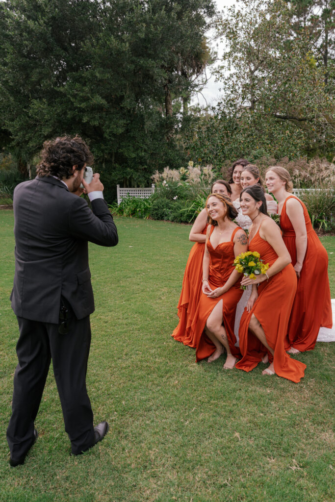 Groom taking a Polaroid photo of bridesmaids in rust-colored dresses during an outdoor Nashville wedding.