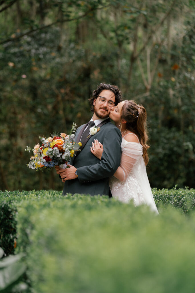 Bride kissing the groom’s cheek while he holds a colorful bouquet during a garden wedding in Nashville.